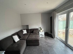 A modern living room with a sectional sofa, a small white side table, and a large sliding glass door leading to an outdoor area.