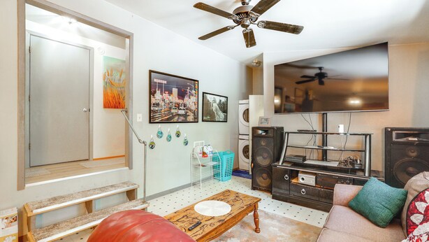 A living room with a sofa, a coffee table, a red leather ottoman, a ceiling fan, a flat-screen TV, and a speaker system. - Next to Wine Rd! Apt w/ Balcony in Fredericksburg (Fredericksburg)