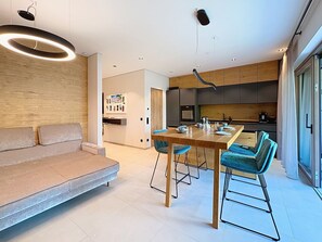 Ein modernes Wohnzimmer mit Sofa, Esstisch mit Stühlen und einer Küchenzeile mit Holzschränken und einer Arbeitsfläche.