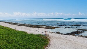 A coastal beach with a clear sky, waves, and a path leading to the water.