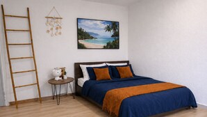 A bedroom with a bed, a wooden ladder, a small round table with a plant, and a wall-mounted picture of a beach.