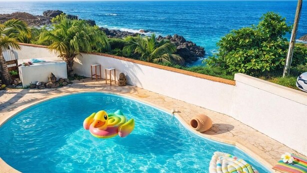 A swimming pool with a view of the ocean, surrounded by greenery and a white wall.