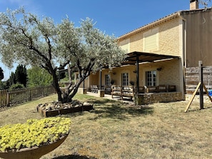 A stone building with a covered patio, outdoor seating, and a large tree.