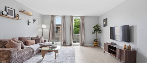 A modern living room with a sofa, coffee table, TV, and a large window with curtains.