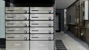A row of metallic, numbered lockers with knobs, likely for storage or mail, in a modern building with tiled walls and a visible water pipe. - Zenith Nishinakanobu 2 (Shinagawa)