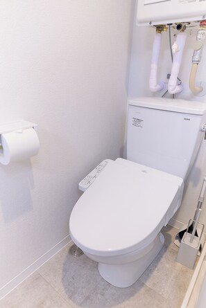 A white toilet with a control panel, a toilet paper holder, and a bidet attachment. - Zenith Nishinakanobu 2 (Shinagawa)