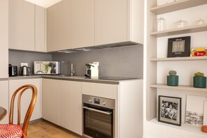 Eine moderne Küche mit weißen Schränken, einem Backofen, einer Mikrowelle und einer Kaffeemaschine. Es gibt eine Essecke mit einem Holztisch und einem Stuhl.