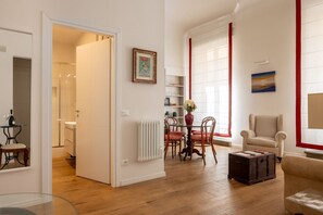 Ein modernes Wohnzimmer mit Essbereich, Holzboden, Heizkörper und einem großen Fenster mit roten Vorhängen.