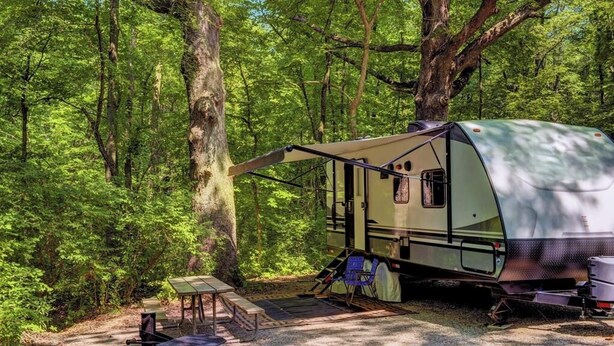 A green RV parked in a forest with a picnic table and a covered area. - The Point At Lake Hartwell (Townville)