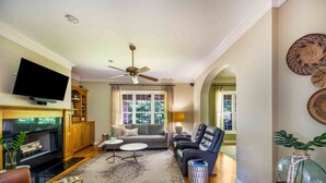 A living room with a fireplace, sofa, television, and ceiling fan. - The Point At Lake Hartwell (Townville)