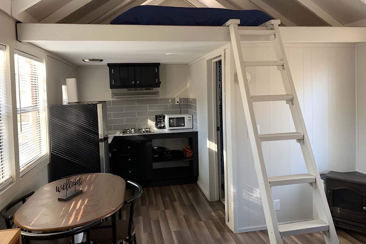 Una cocina compacta con microondas, estufa y armarios, una pequeña mesa de comedor con un cartel de 'Welcome', una escalera y una chimenea.