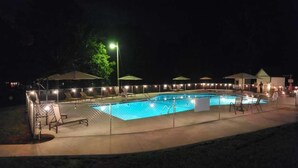 A rectangular swimming pool with a tiled deck, surrounded by lounge chairs and umbrellas, and a covered seating area. - The Point At Lake Hartwell (Townville)