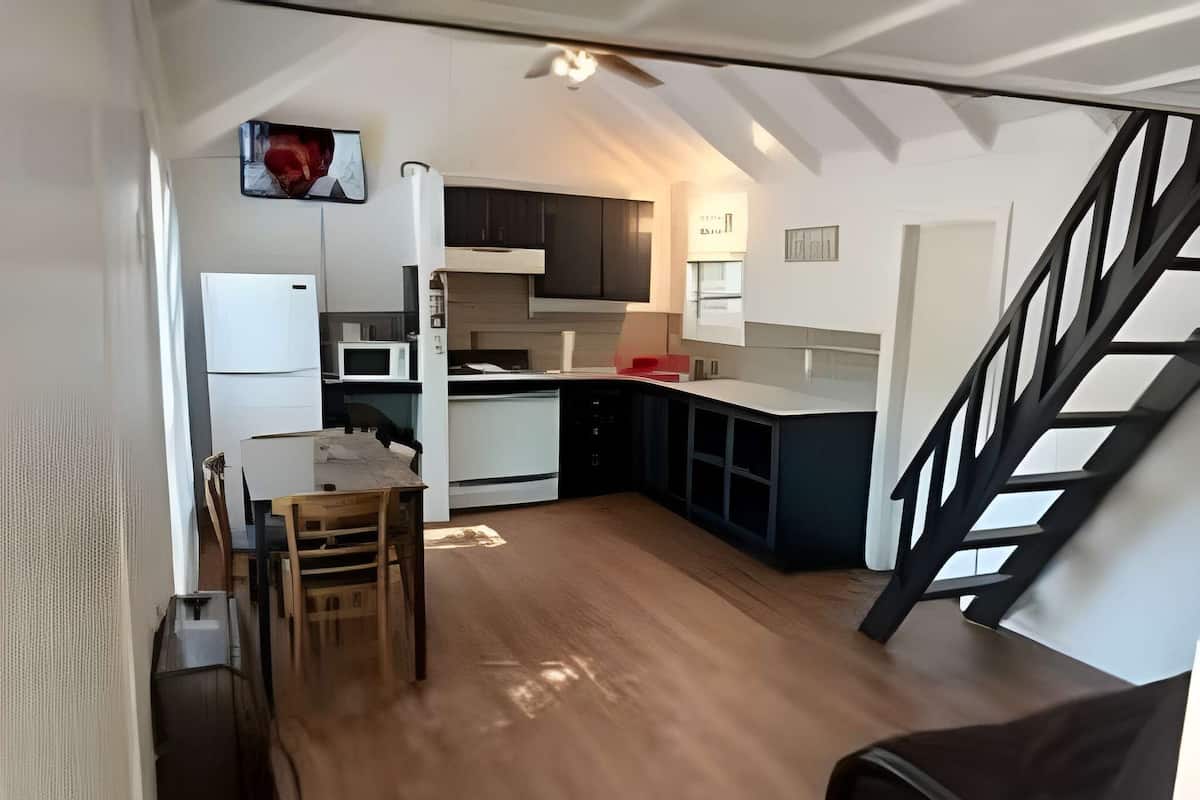 Una cocina compacta con electrodomésticos modernos, un comedor con mesa de madera y una escalera que sube a otro nivel.