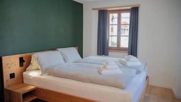 Una habitación con una cama de madera, una mesita de noche, una ventana con cortinas y vistas a edificios.