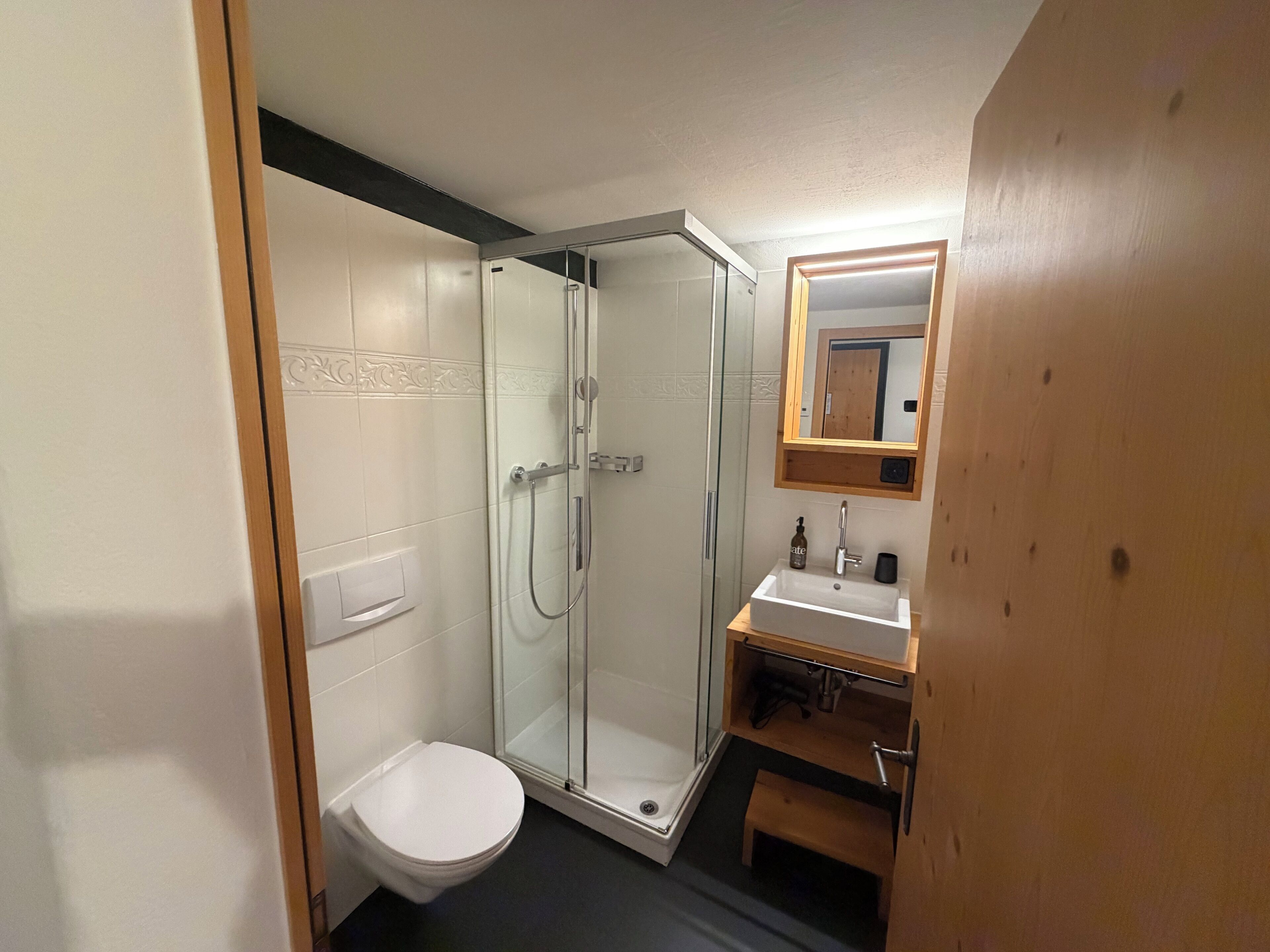 Un bagno con box doccia in vetro, un water bianco, un lavandino con specchio sopra e una panca in legno.