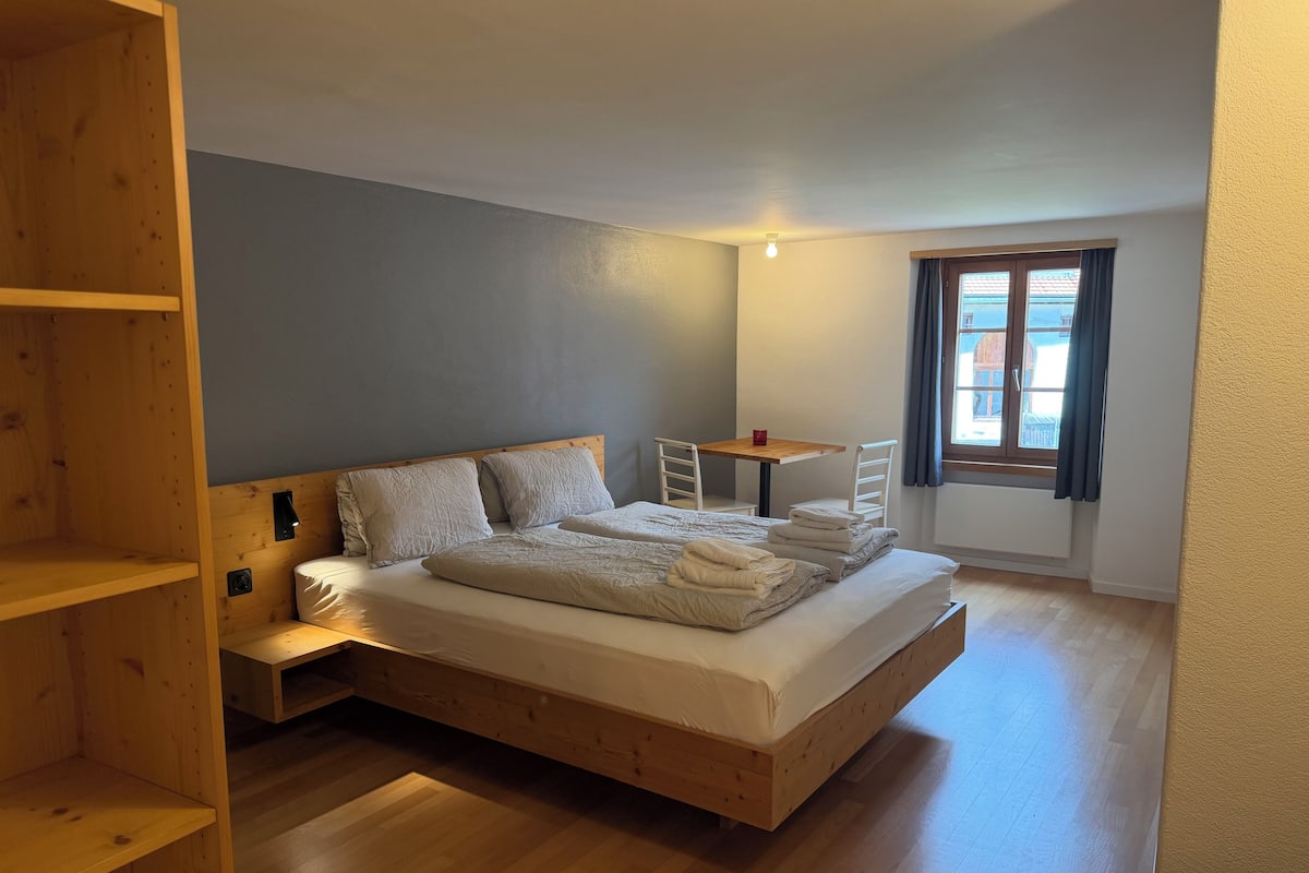 A bedroom with a wooden bed, a small table, and a window with curtains.