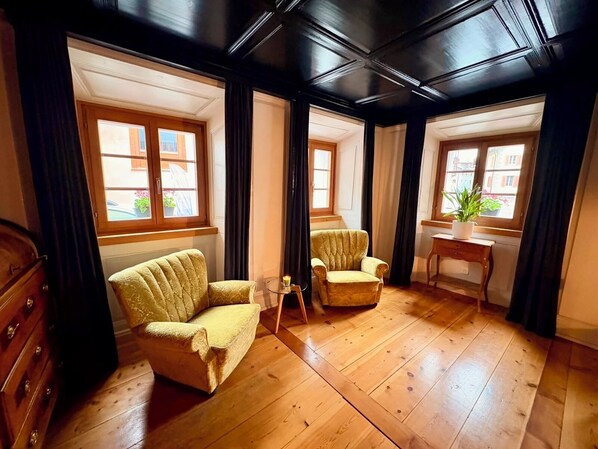 Una habitación con suelo de madera, dos sillones, una mesita y un escritorio con planta en maceta.