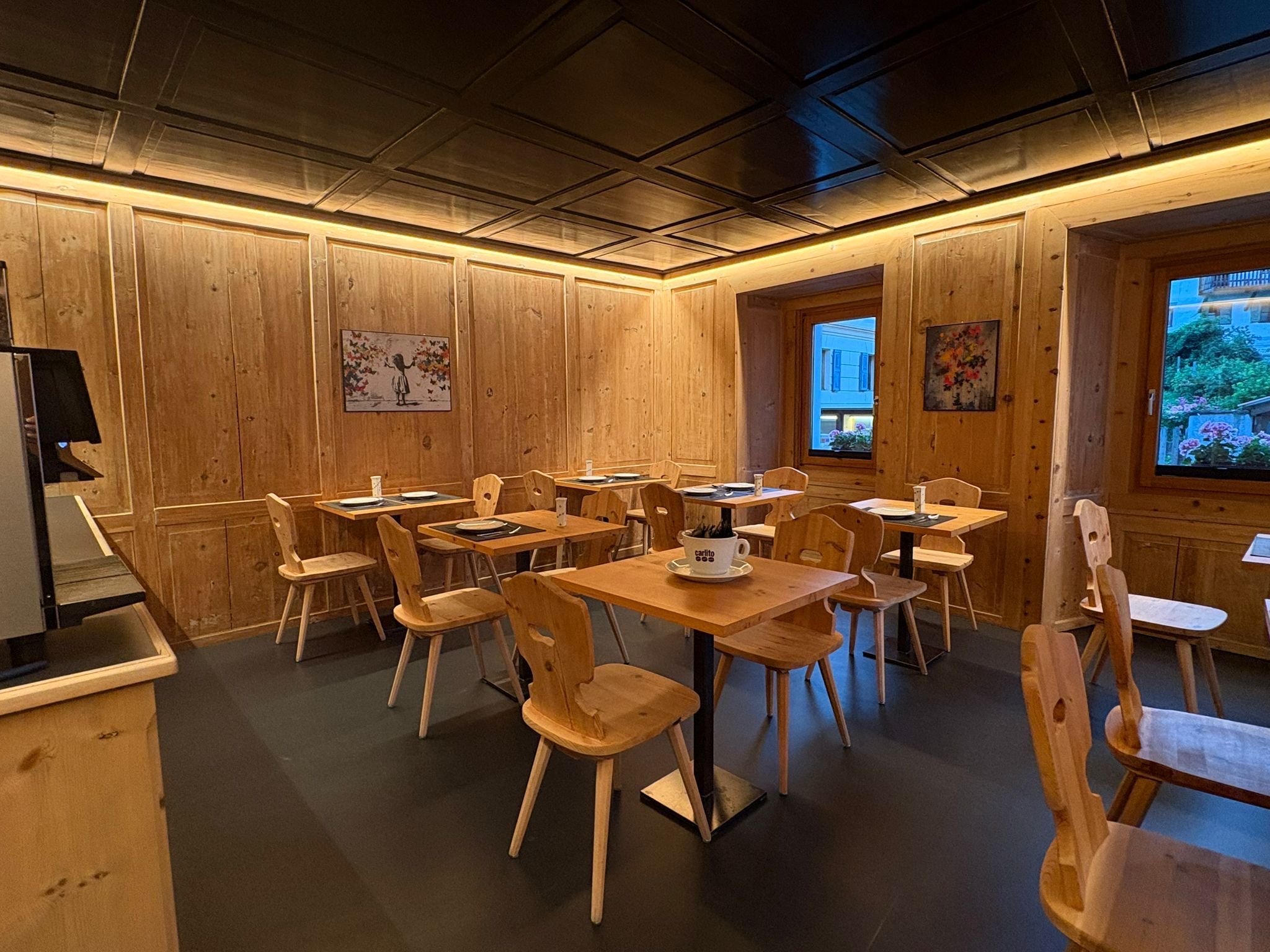 Um restaurante acolhedor com paredes e mesas de madeira, com obras de arte e uma janela com vista.