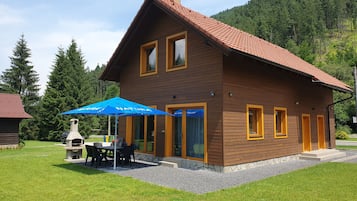 A wooden house with a red-tiled roof, a patio with outdoor seating, and a stone fireplace.