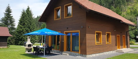Uma casa de madeira com telhado de telhas vermelhas, um pátio com área de estar externa e uma lareira de pedra.