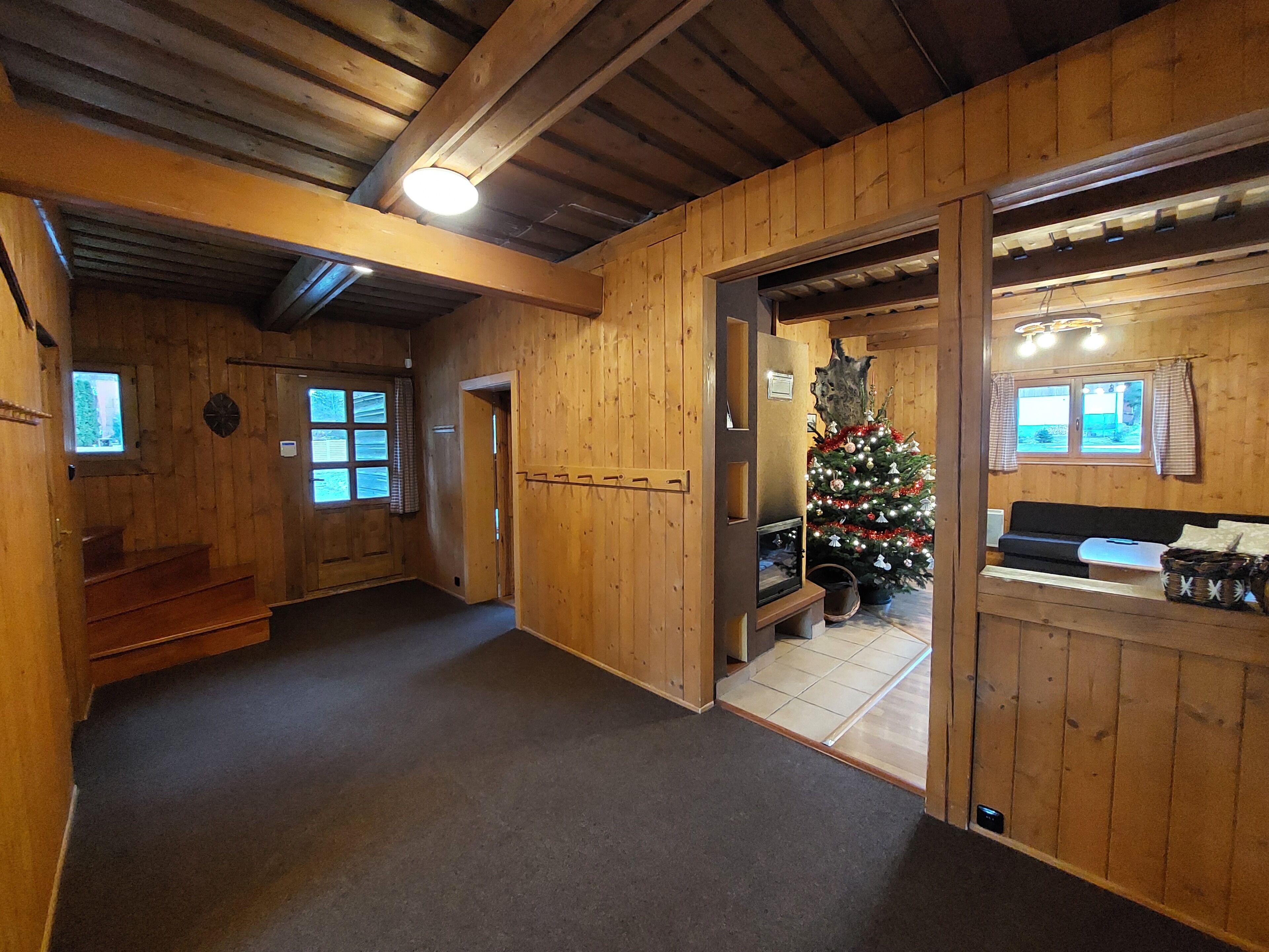 A wooden interior with a Christmas tree, a fireplace, and a sofa.