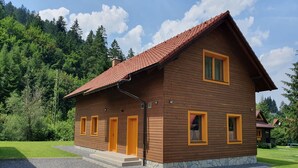 A two-story wooden house with a red-tiled roof, multiple windows with yellow frames, and a stone foundation. - Chalets Hana (Demänovská Dolina)