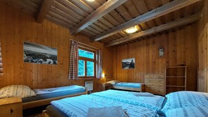 A wooden cabin room with two beds, a dresser, a window with curtains, and a wall-mounted heater. - Chalets Hana (Demänovská Dolina)