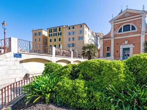 A stone bridge with a sign reading "Place Mere Teresa," surrounded by lush greenery and historic buildings with balconies and a church with a dome. - Apartment Diana by Interhome (Ajaccio)