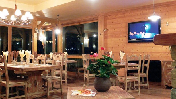 Un interior de madera con comedor, un televisor montado en la pared y un ventanal grande.