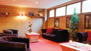 Una habitación acogedora con una pared de madera, un sofá, sillones, una mesita con un florero y una planta en maceta.