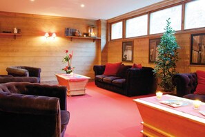 Une pièce chaleureuse avec un mur en bois, un canapé, des fauteuils, une petite table sur laquelle est posé un vase, et une plante en pot.