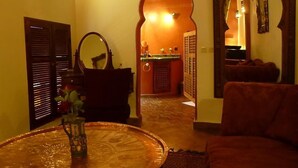 Un interior de estilo marroquí con una mesa redonda, un sofá y un arco que da a una zona de cocina.