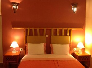 Habitació d'hotel amb un llit, dues làmpades laterals i una llum penjada a la paret.