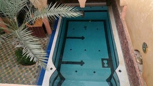 Una piscina con piso azul, rodeada por un área empavedada con plantas de palma.