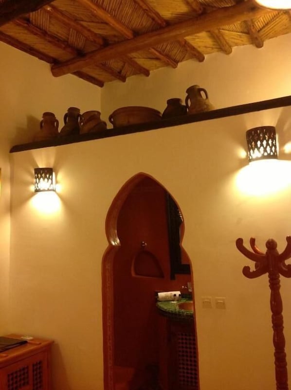 Una habitación con techo de madera, una repisa con cerámica, luces empotradas en la pared y una puerta en arco.