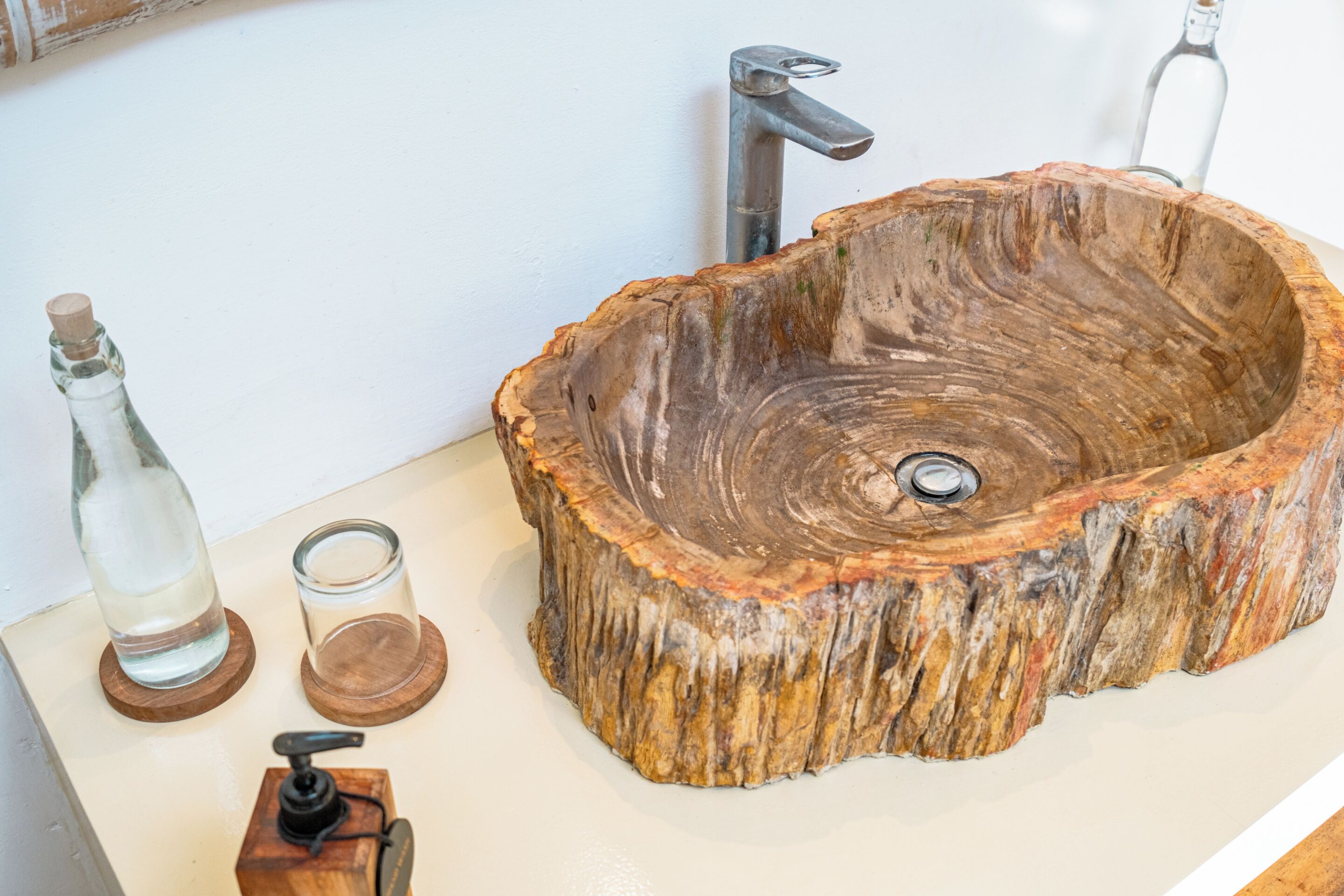 Ein Waschbecken aus Holz mit einem Wasserhahn, einer Glasflasche und einer Holzpumpe.