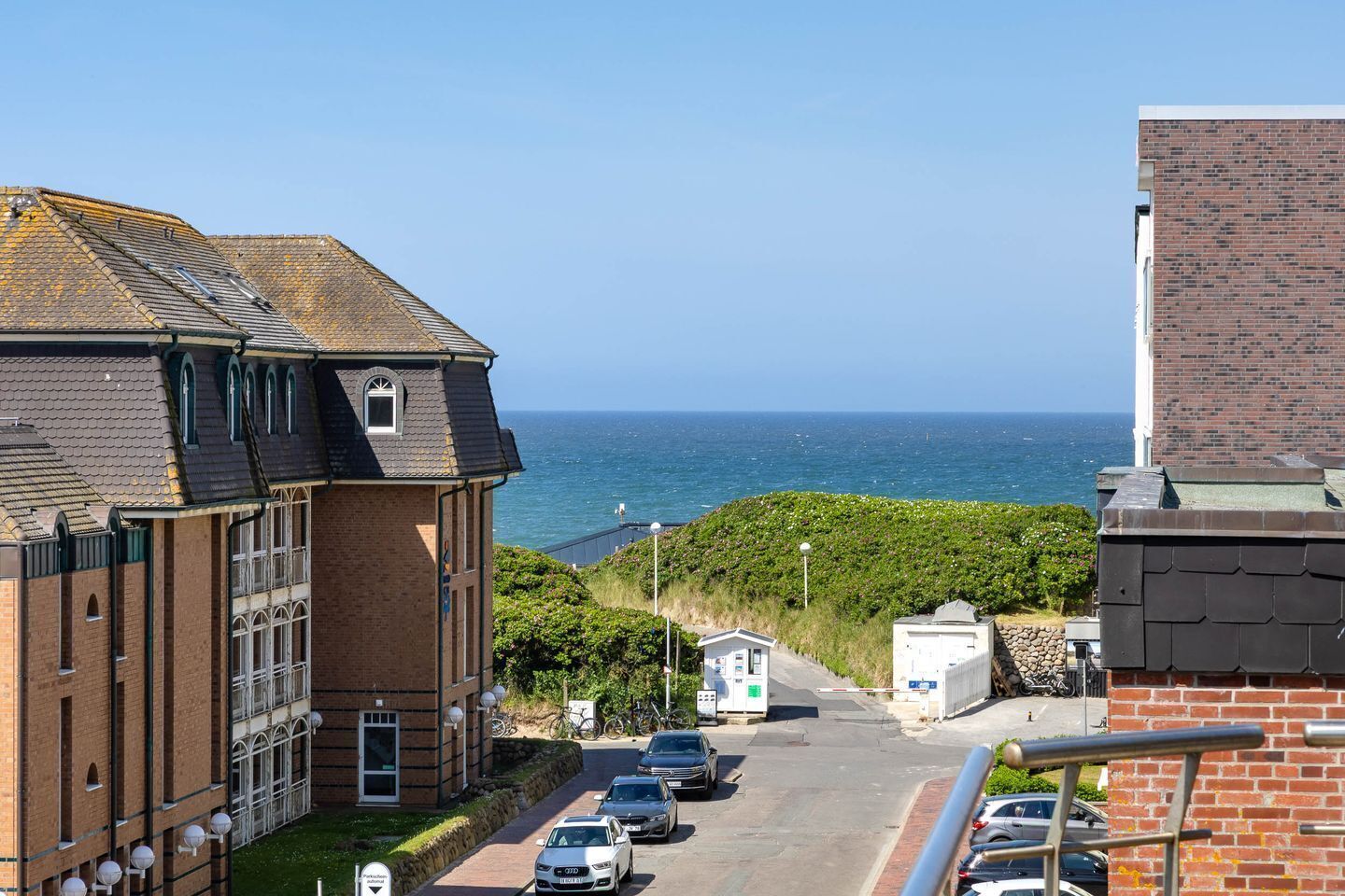 A coastal building with a view of the sea, a parking area, and a bike path.