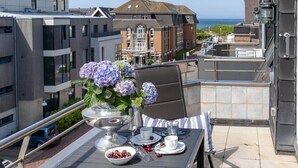 Terraço no telhado com uma mesa posta para dois, área de estar ao ar livre e vista para o mar e edifícios.