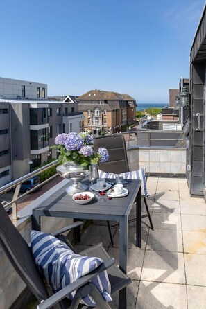 Eine Dachterrasse mit Tisch für zwei Personen, Außenbereich zum Sitzen und Blick auf das Meer und Gebäude.