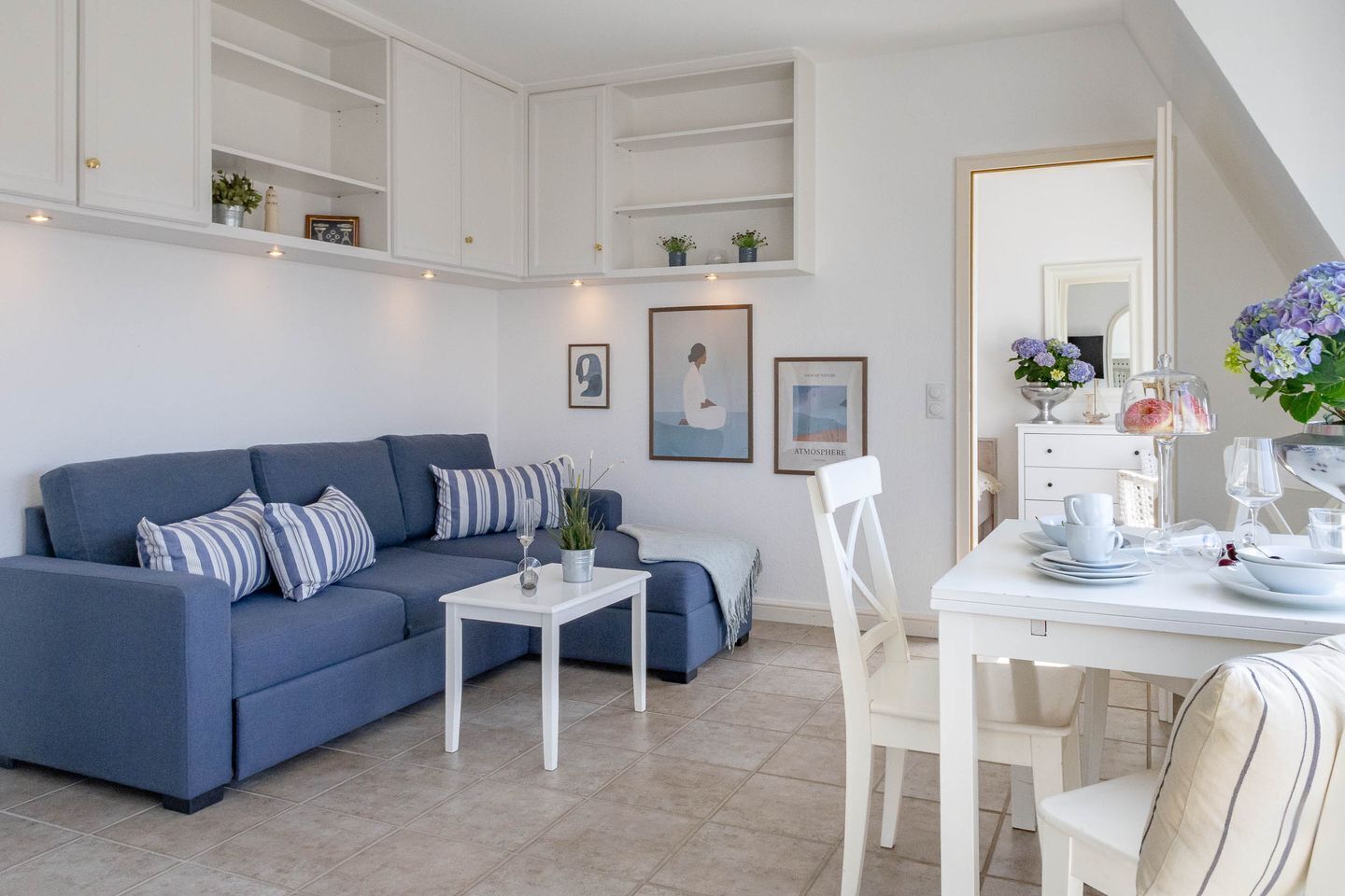 Una sala de estar moderna con un sofá azul, una mesa de centro blanca y un comedor con platos y vasos.