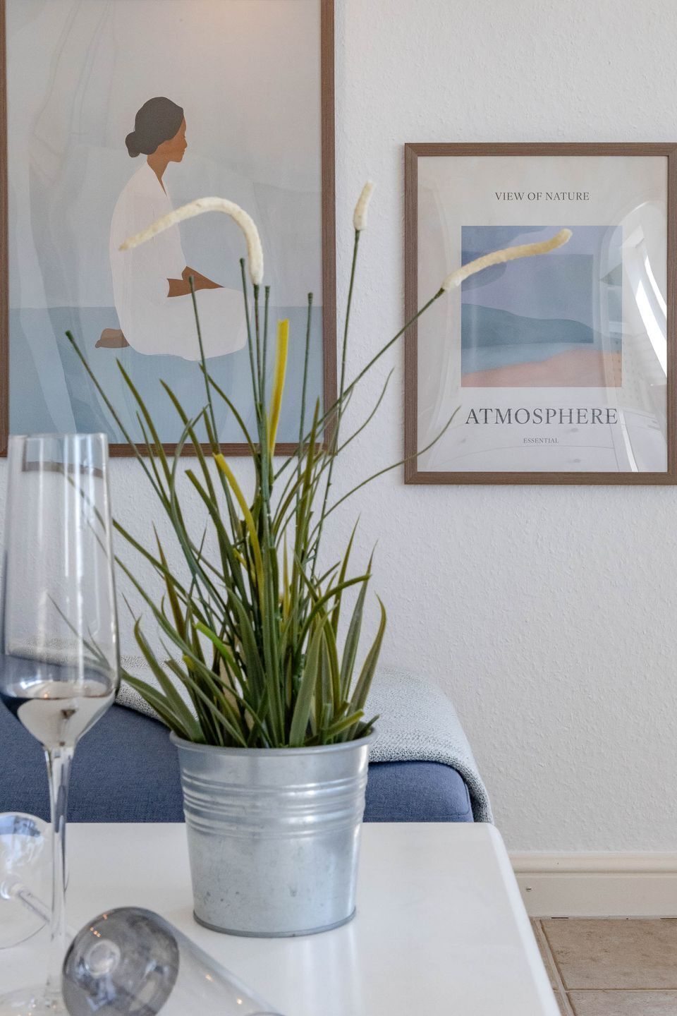 Une plante en pot est posée sur une table, à côté d’un tableau encadré et d’un verre.