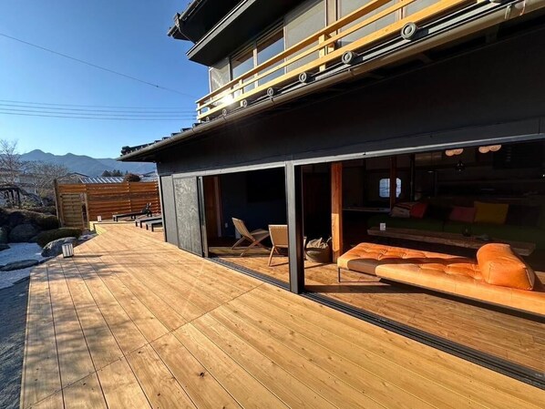 A modern building with a wooden deck, outdoor seating, and a view of mountains.