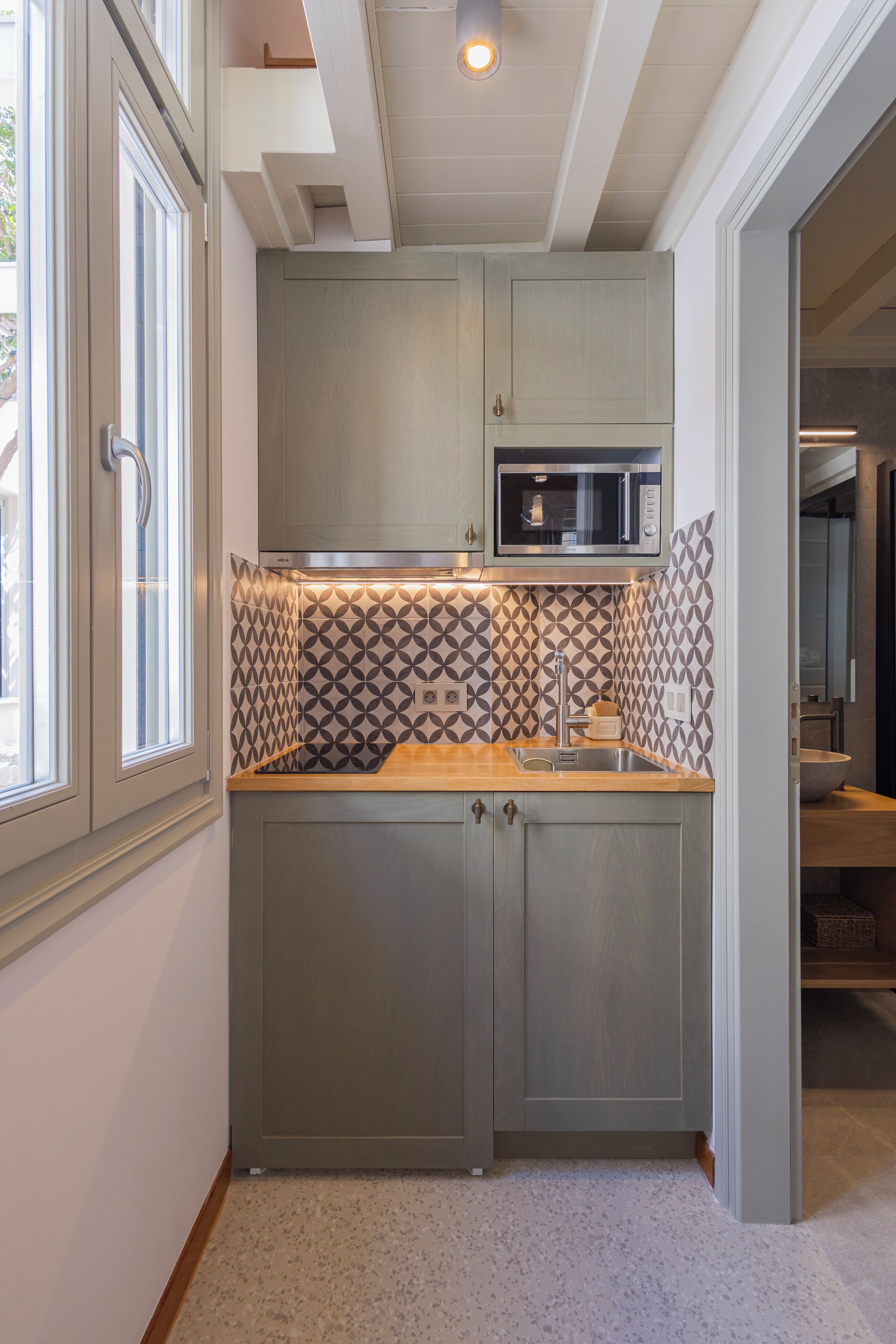 A kitchen with grey cabinets, a microwave, and patterned backsplash.