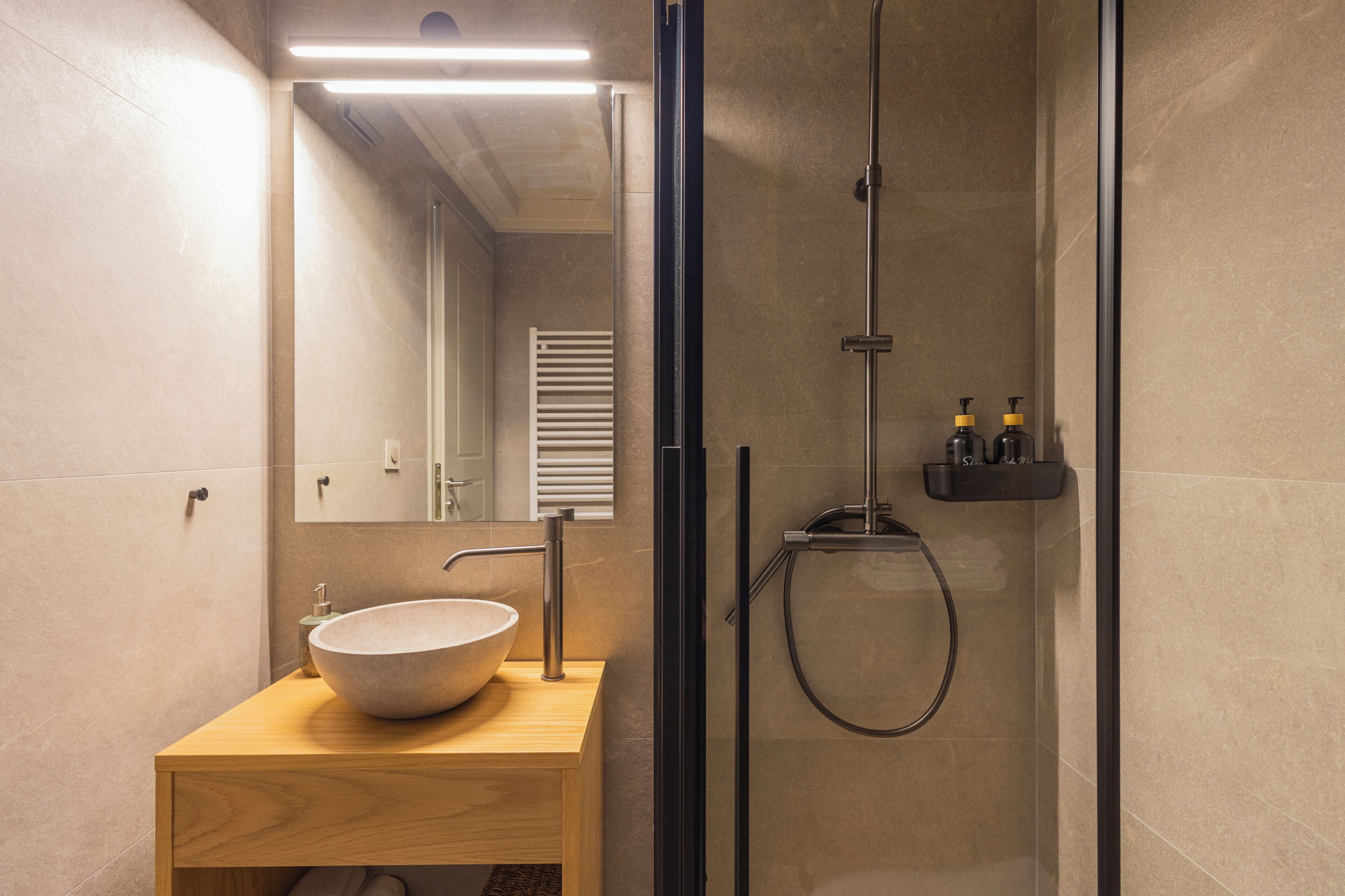 A modern bathroom with a wooden vanity, a large vessel sink, a glass-enclosed shower, and a mirror.