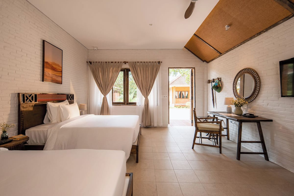 Habitación de hotel con dos camas, un escritorio, una silla, un espejo y vistas al exterior.
