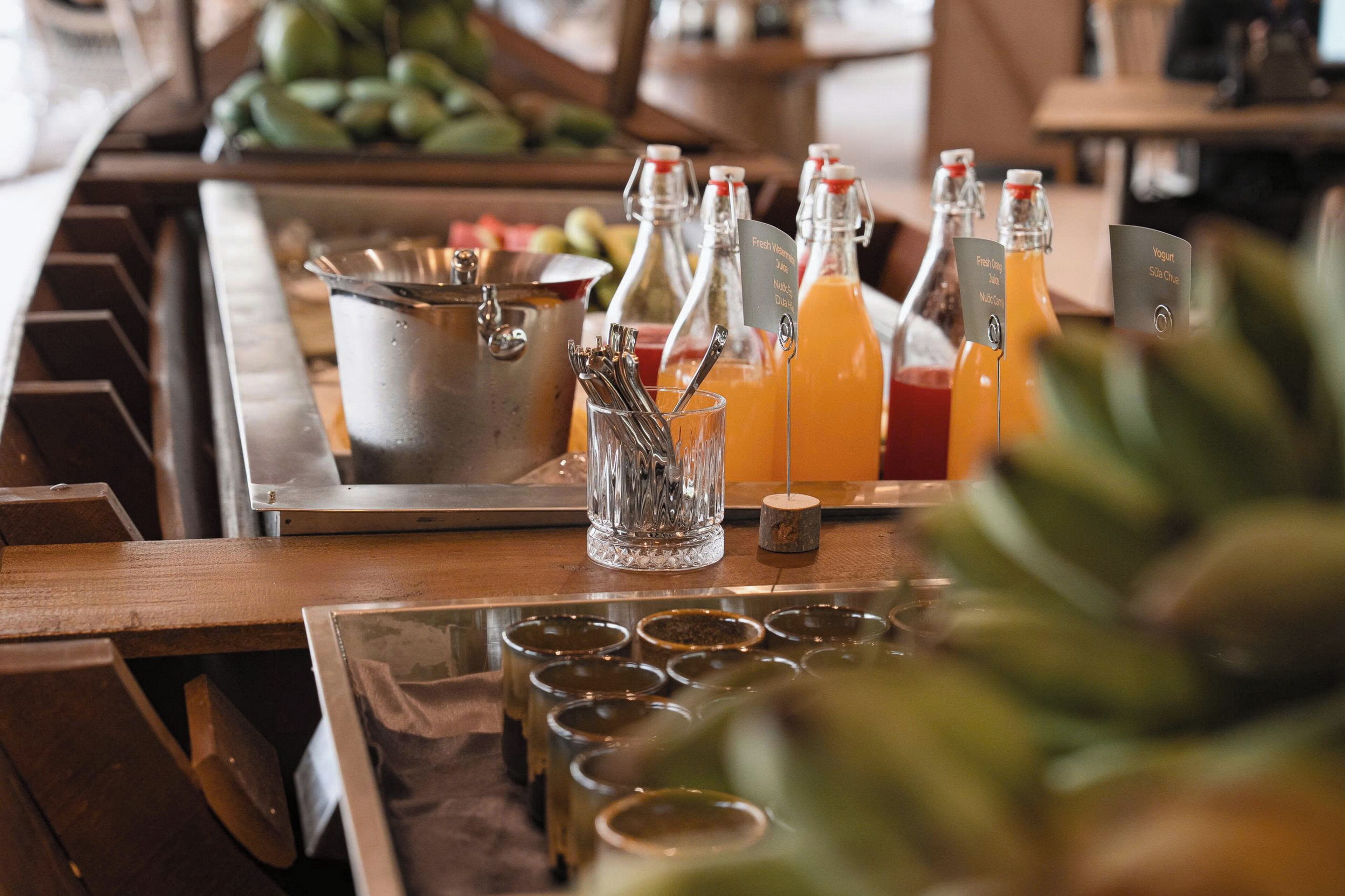 A bar area with a variety of beverages, including fresh juice and yogurt drinks, and a metal container with utensils.