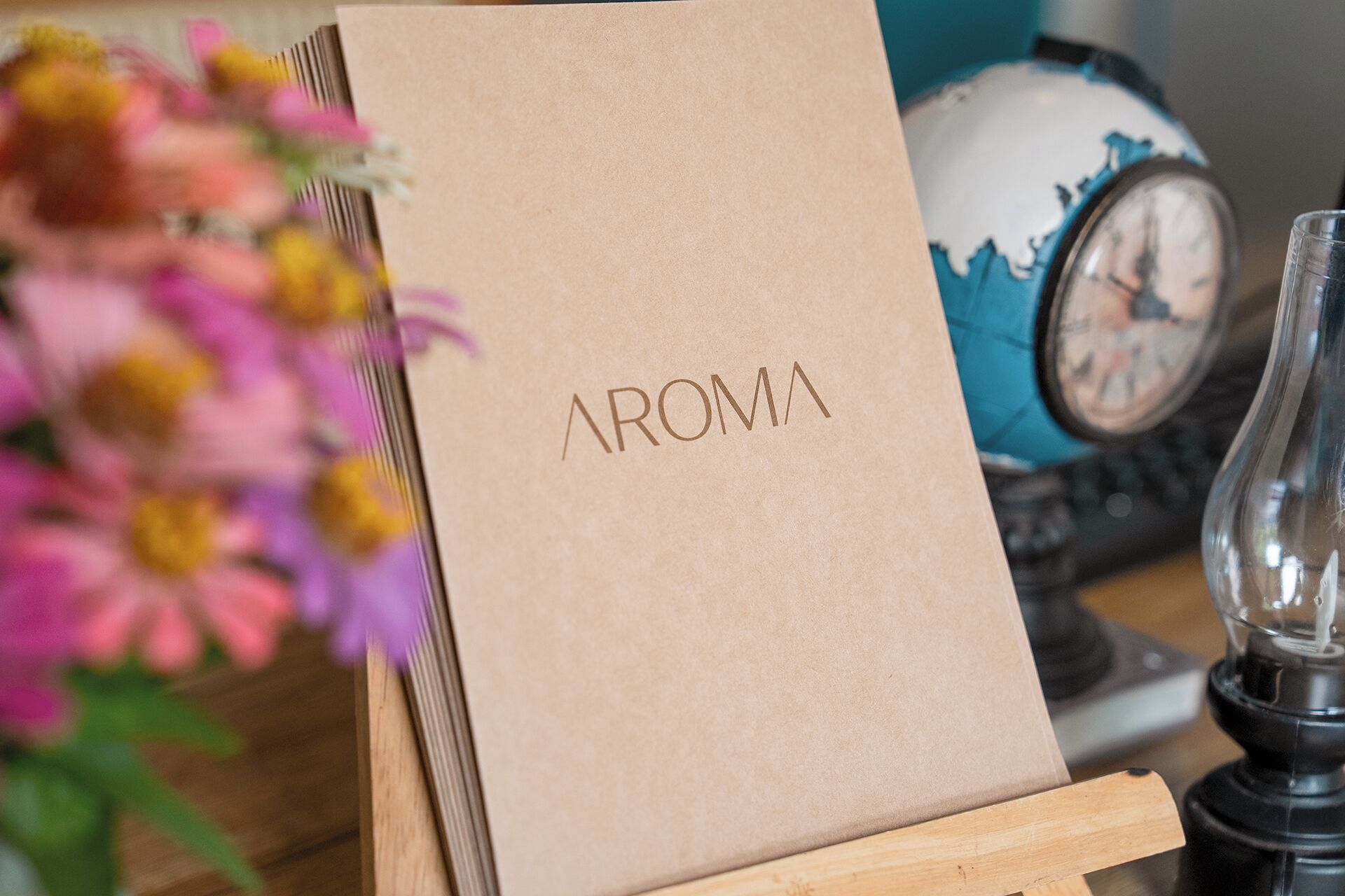A brown paper bag with 'AROMA' printed on it, placed on a wooden stand.