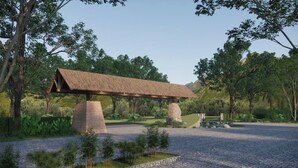 Un banco de piedra con techo de paja en un jardín ajardinado con árboles y un estanque.