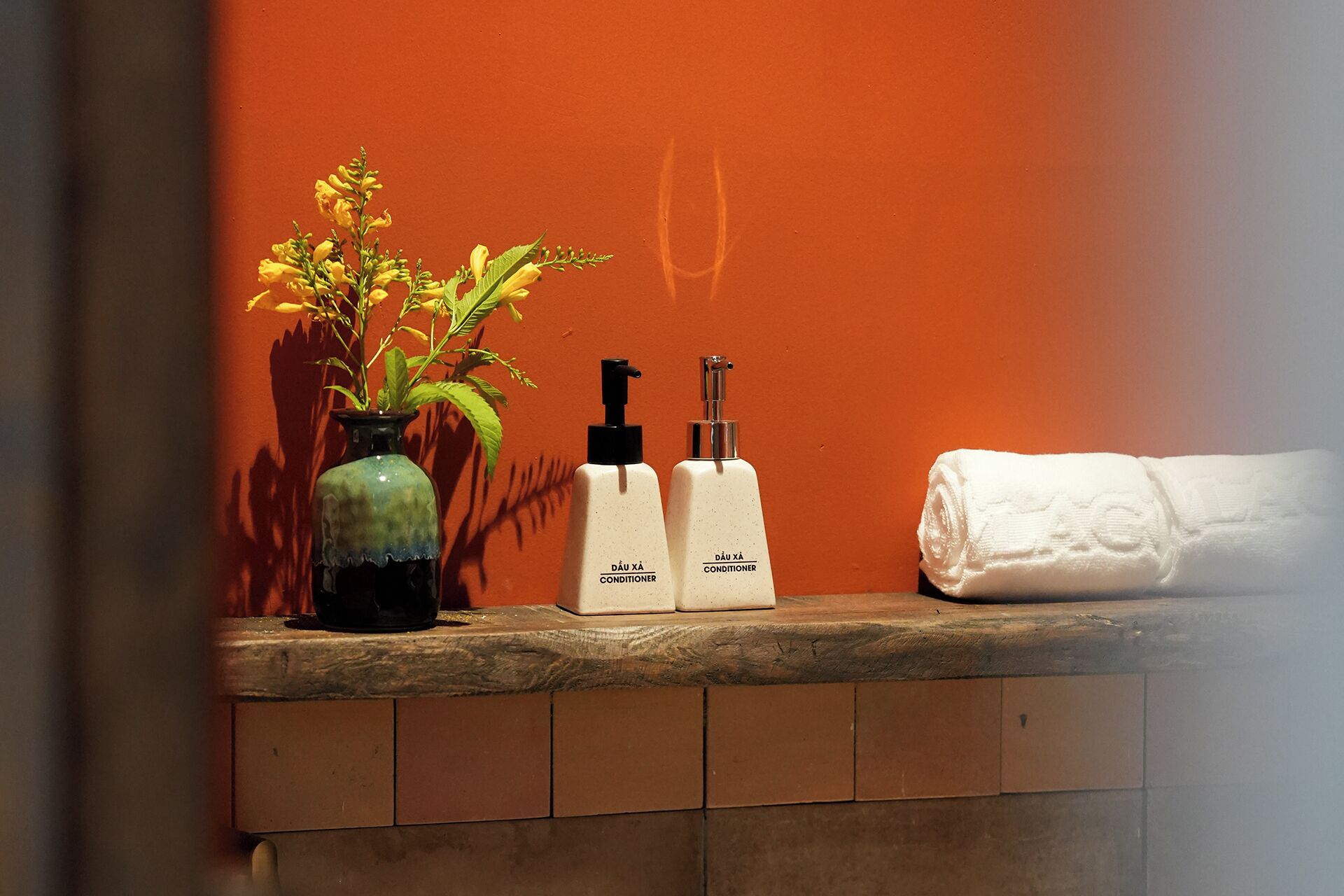 A bathroom counter with a vase of yellow flowers, two white conditioner bottles, and a rolled white towel.