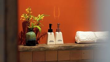 A bathroom counter with a vase of yellow flowers, two white conditioner bottles, and a rolled white towel.